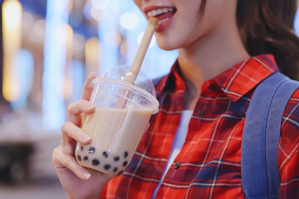 Woman drinking boba tea through a straw and smiling